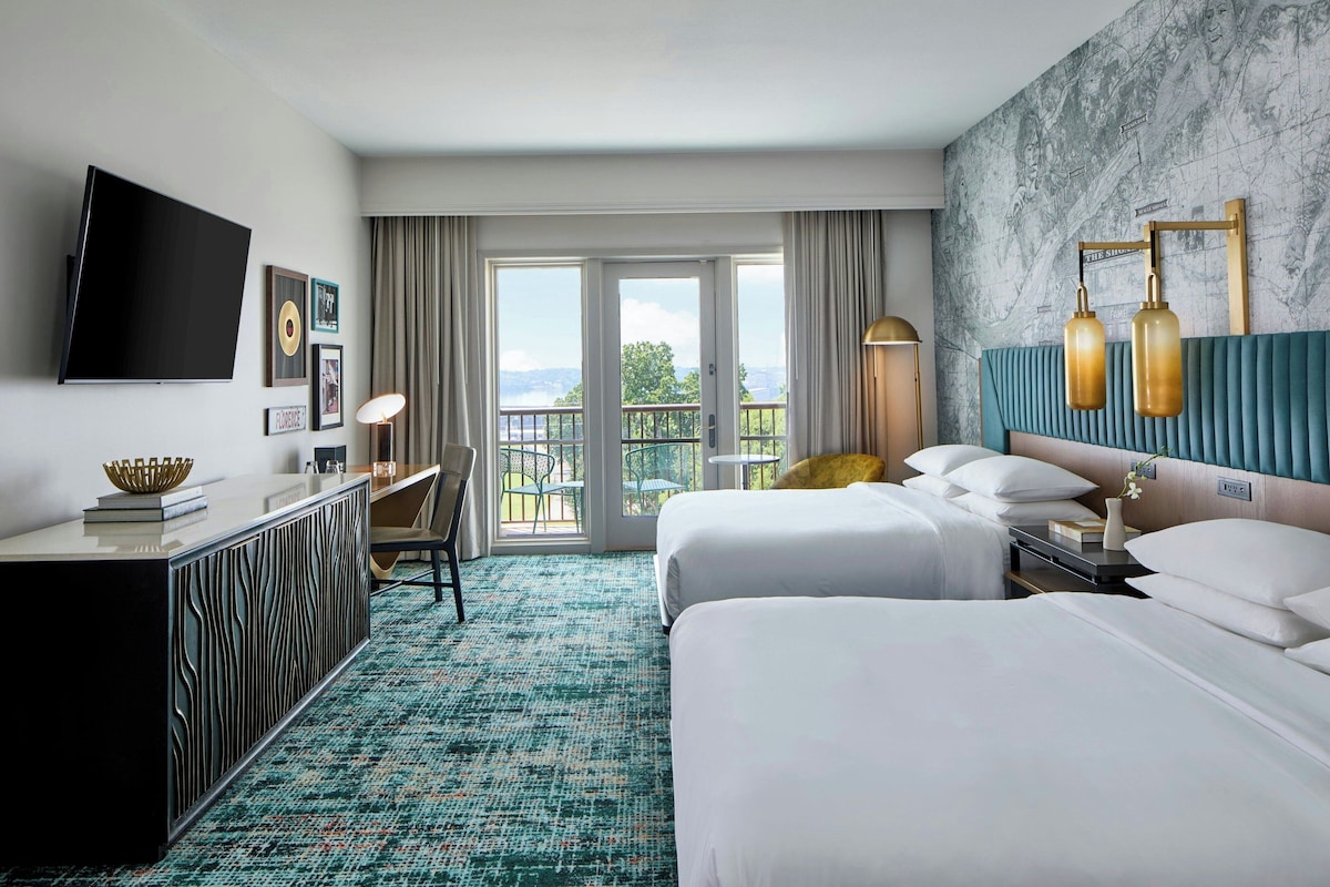 Una habitación de hotel con dos camas, un escritorio, un televisor y un balcón con vistas.