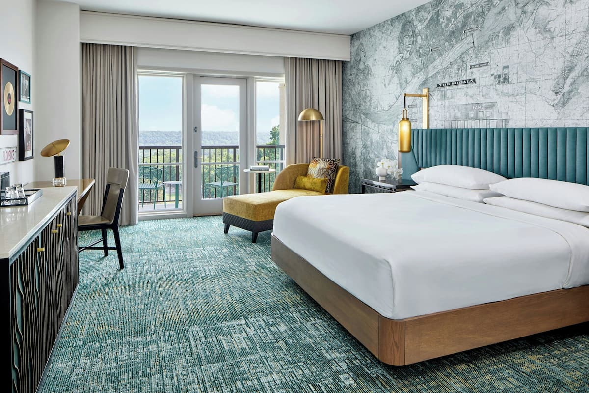 A hotel room with a large bed, a desk, a chair, a balcony with a view, and a map on the wall.
