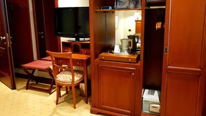 Une pièce de taille modeste, comprenant un bureau en bois, une chaise, un téléviseur, un placard et un petit coin cuisine.