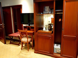 Ein kleines Zimmer mit Holzschreibtisch, Stuhl, Fernseher, Schrank und einer kleinen Küchenzeile.