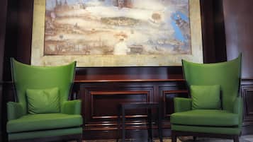 Un hall d’entrée avec deux fauteuils verts, une petite table et un grand tableau abstrait accroché au mur.