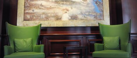 A lobby with two green armchairs, a small table, and a large abstract painting on the wall.
