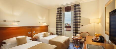 A hotel room with two beds, a desk with a laptop, a TV, and a window with curtains.