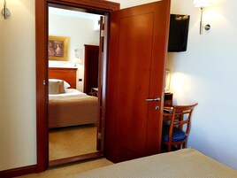 Habitación de hotel con puerta de madera, una cama, un escritorio con silla y un televisor montado en la pared.