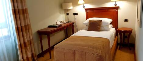 A hotel room with a bed, bedside tables, lamps, a desk, and a window with curtains.