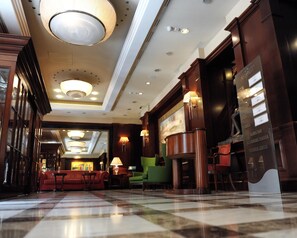 Un hall d’hôtel avec un sol à carreaux, un grand lustre et un comptoir d’accueil.