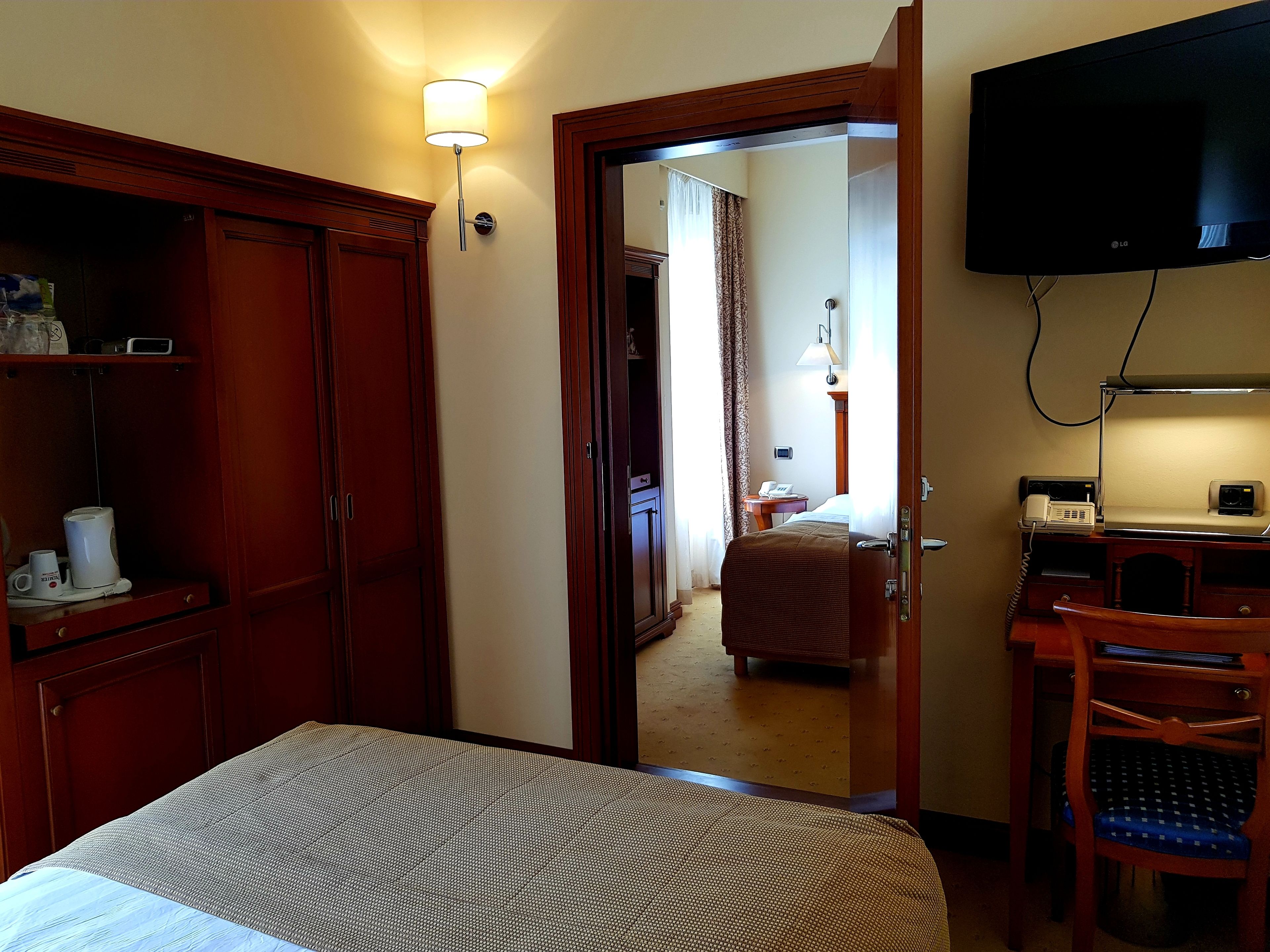 A hotel room with a bed, wardrobe, desk, chair, and a television.