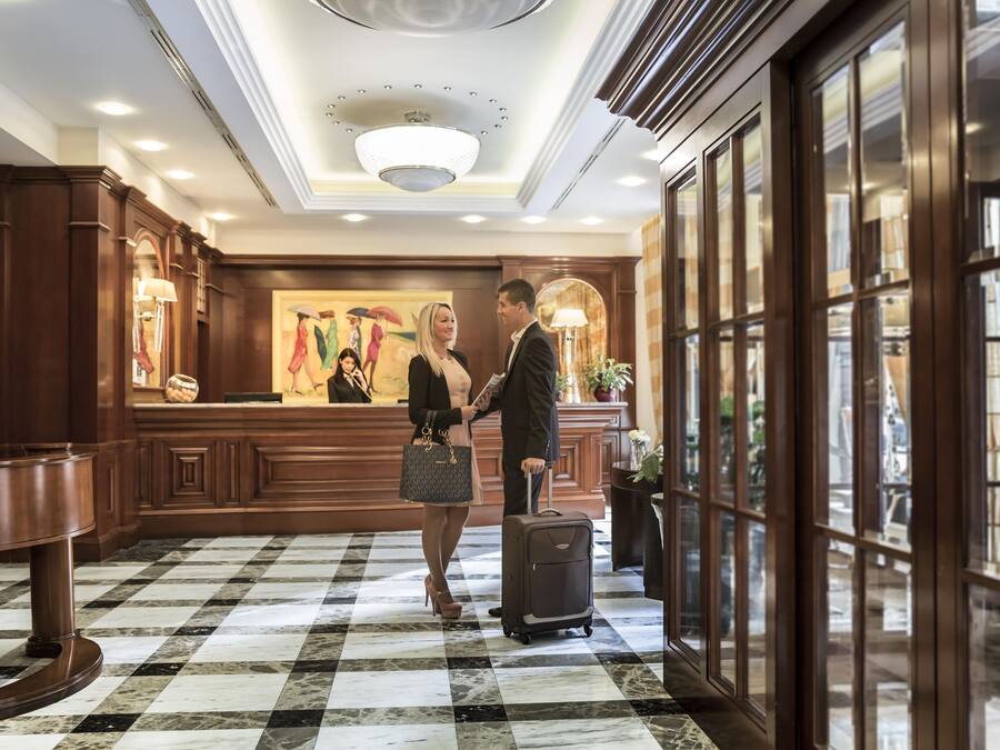 A lobby with a checkered floor, a reception desk, and a painting of people with umbrellas.