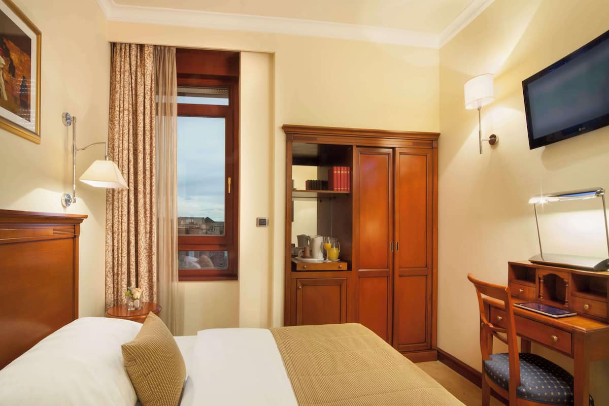 A hotel room with a bed, a desk, a chair, a wardrobe, a television, and a window with curtains.