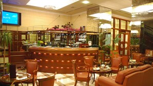 Un hall d’hôtel comprenant un bar, des espaces aménagés avec des sièges et un écran de télévision affichant le mot « SUITE ».