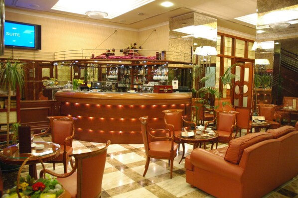 A hotel lobby with a bar area, seating arrangements, and a television screen displaying "SUITE".