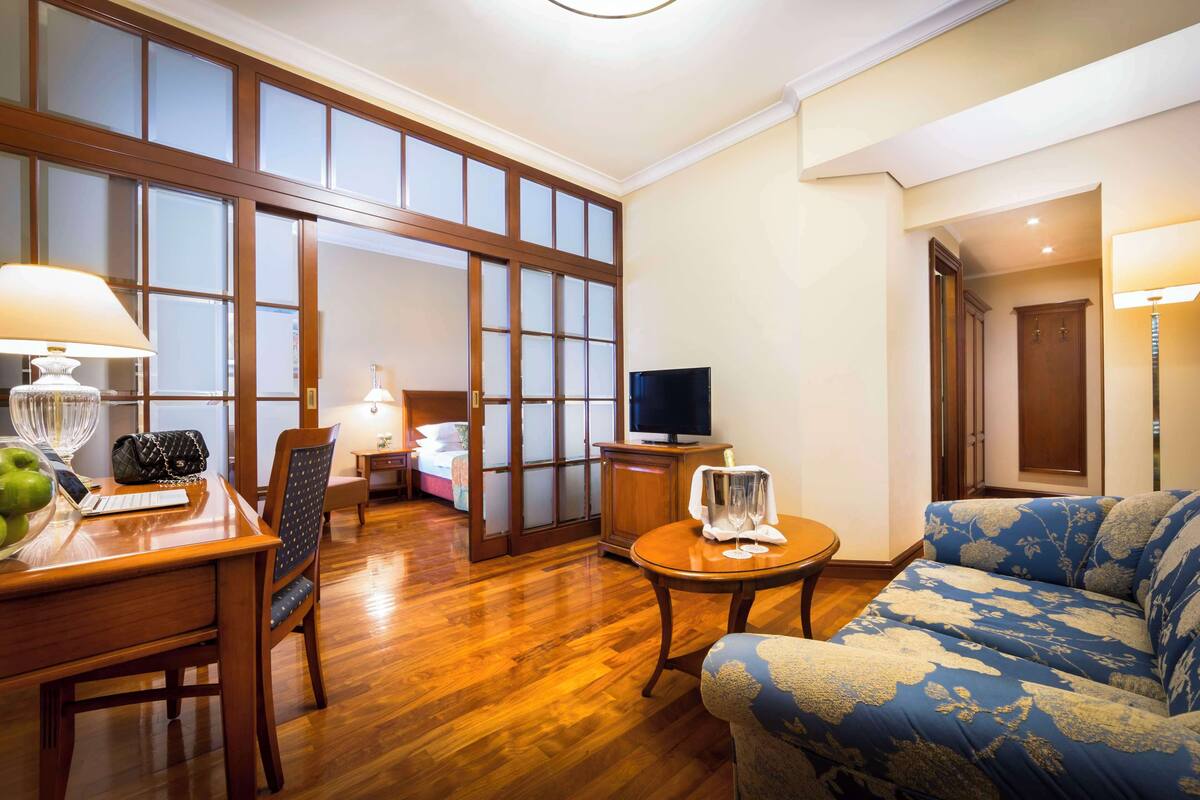 A spacious living room with wooden flooring, a sofa, a television, and a dining area with a table and chairs.