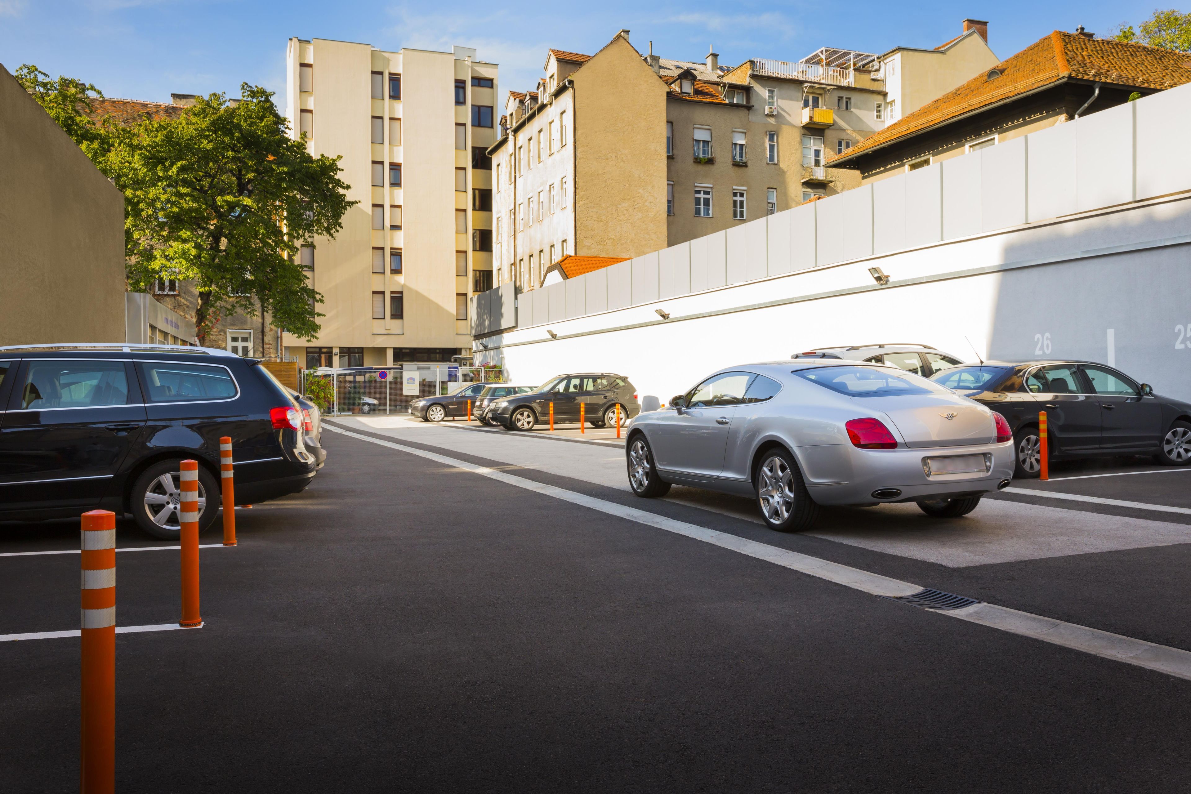 Un estacionamiento con varios coches, una pared blanca y edificios al fondo.