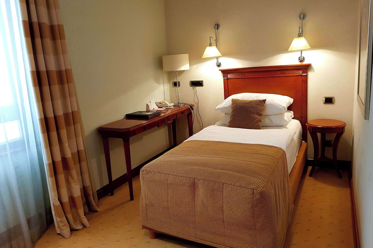 A hotel room with a bed, a desk, two bedside lamps, a telephone, and a small table.