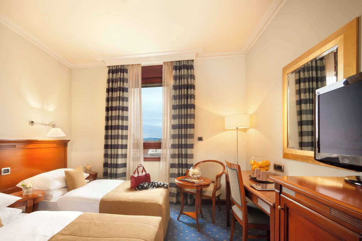 A hotel room with two beds, a desk with a chair, a TV, and a window with curtains.