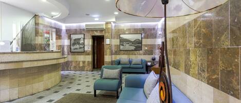 A lobby with a curved reception desk, a blue sofa, a patterned rug, and a large floor lamp.