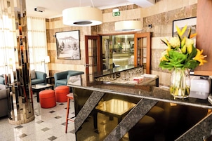 Un vestíbulo de hotel con mostrador de recepción, zona de estar y un espejo grande.
