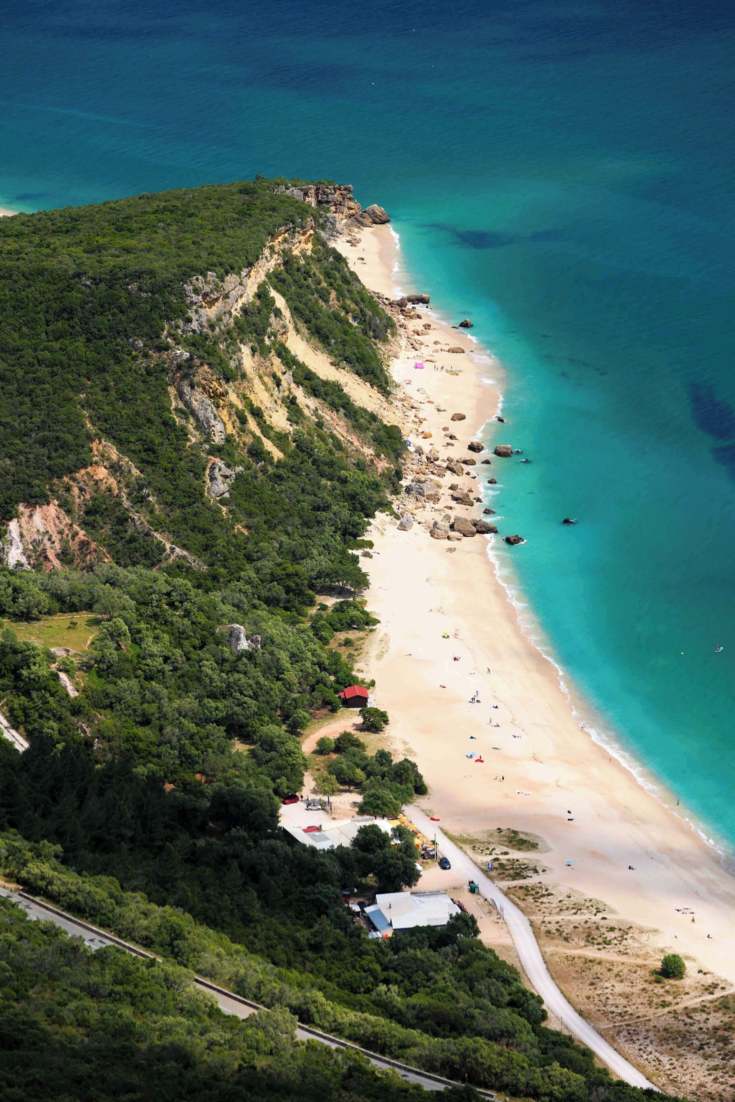 Vista aérea de una zona costera con playa de arena, abundante vegetación y mar azul transparente.