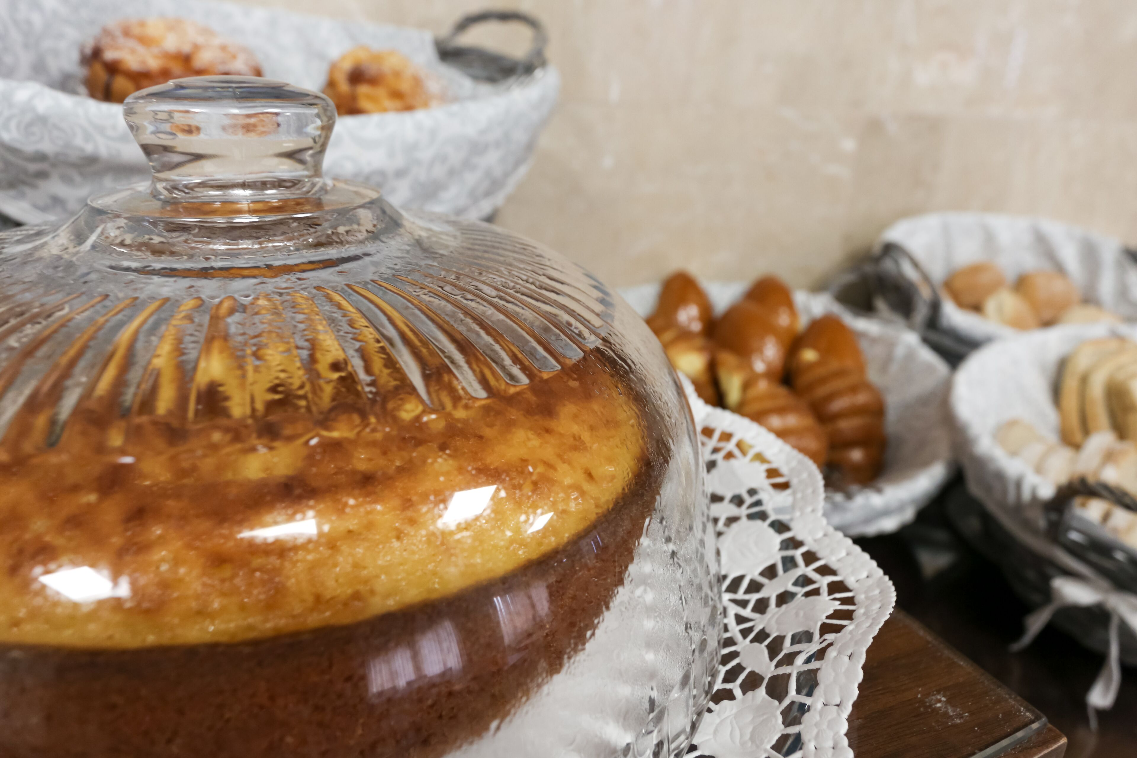 A dessert display with a glass dome cover, a lace doily, and various pastries in baskets.