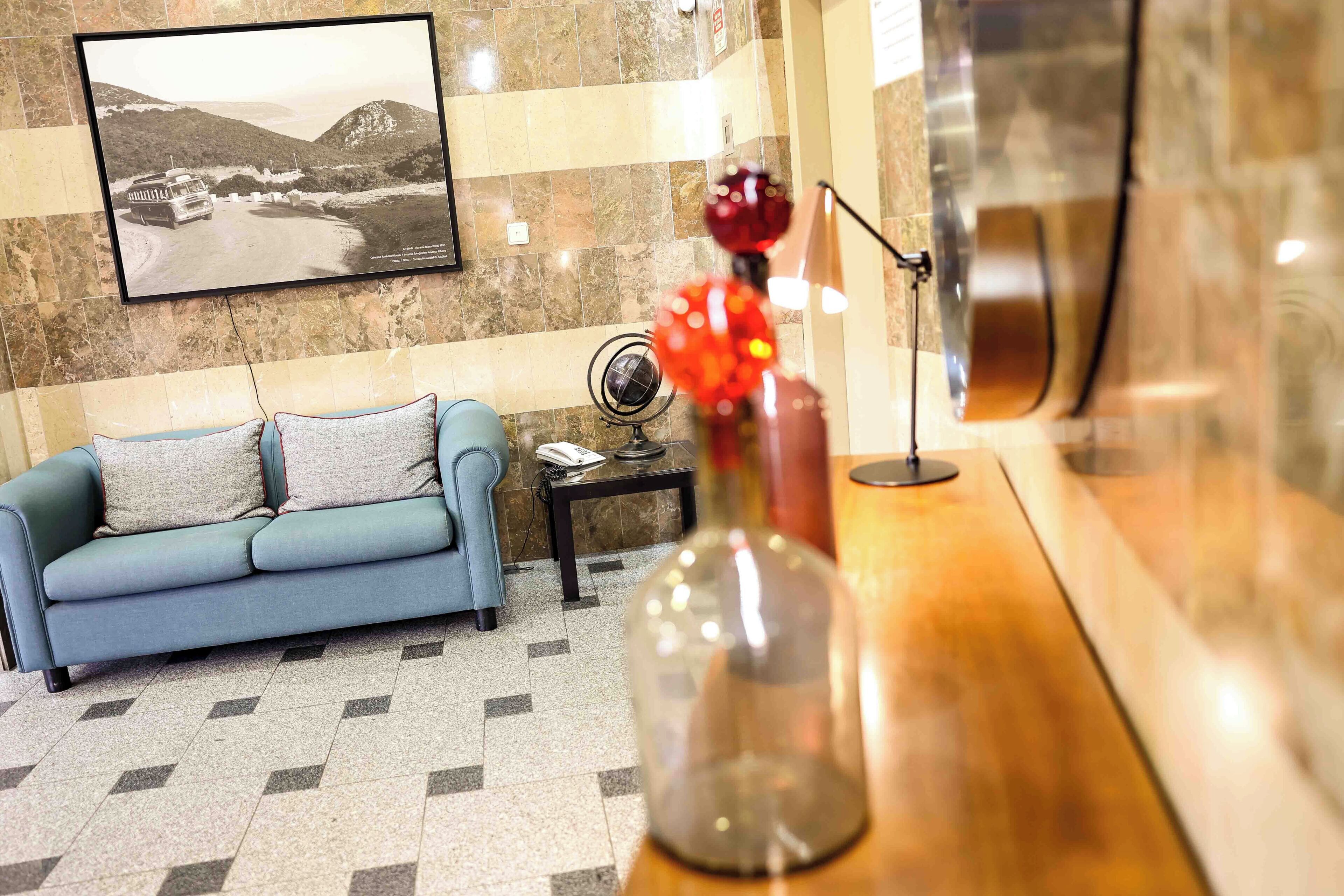 A hotel lobby with a blue sofa, a small table with a globe and a vase, and a framed picture on the wall.