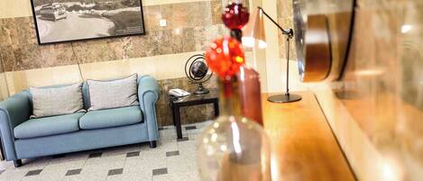 A hotel lobby with a blue sofa, a small table with a globe and a vase, and a framed picture on the wall.