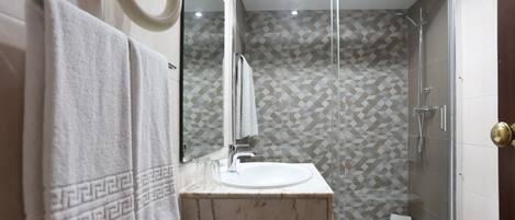 Un baño moderno con ducha de vidrio, lavamanos de mármol y un espejo grande.
