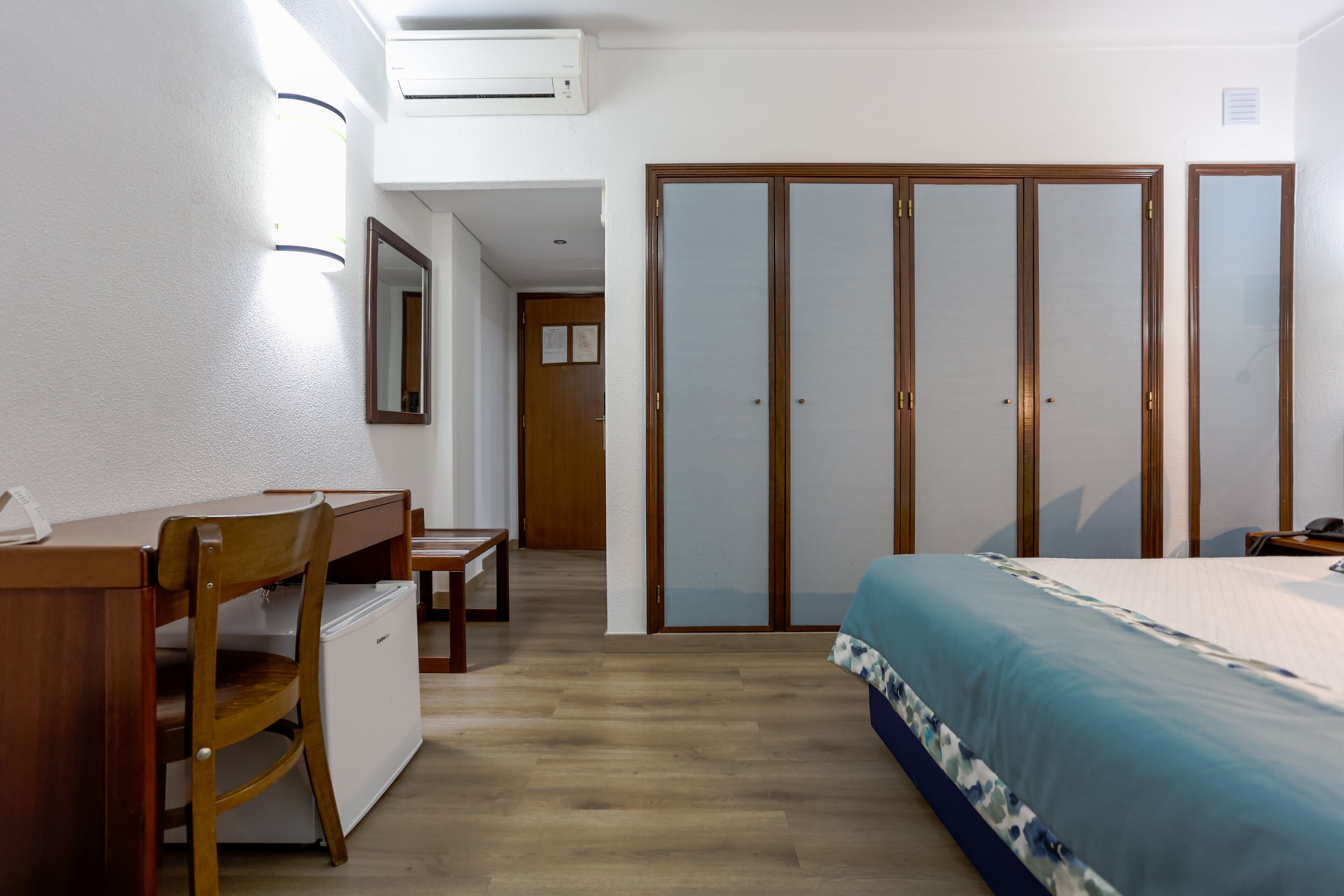 Een slaapkamer met een bed, een bureau, een stoel, een kledingkast en een kleine tafel.