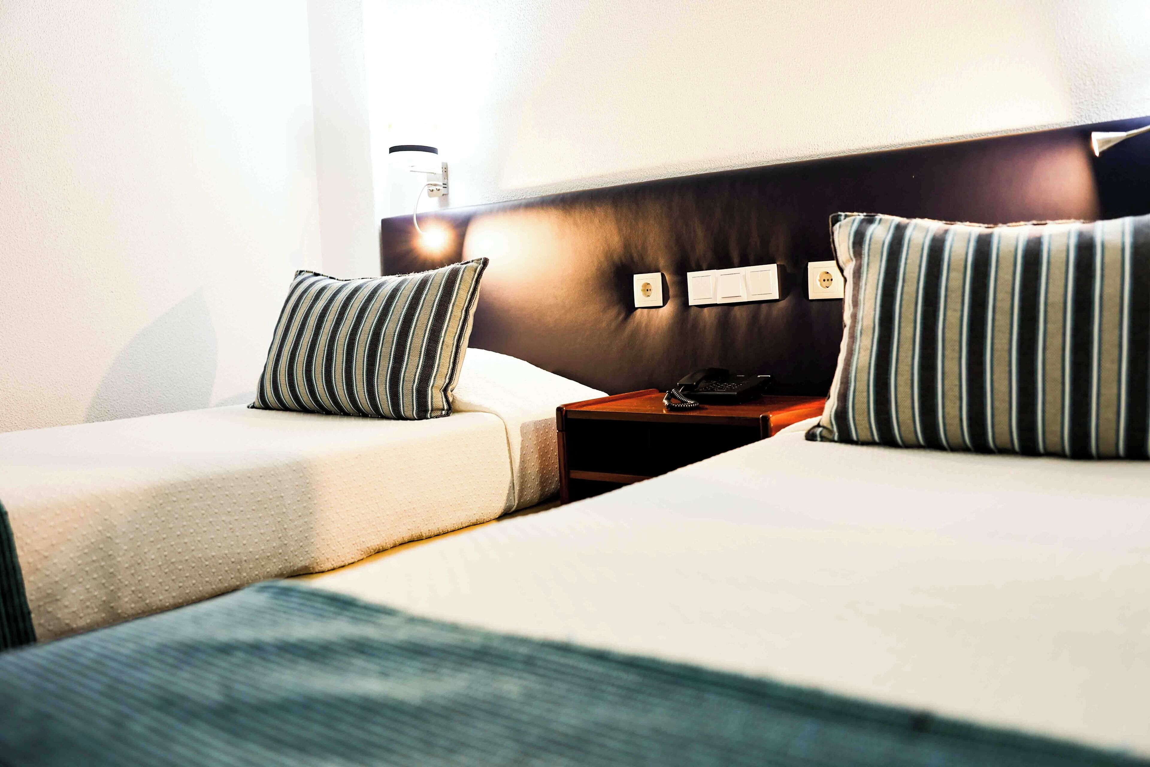 A hotel room with two beds, a bedside table with a phone, and a wall socket.