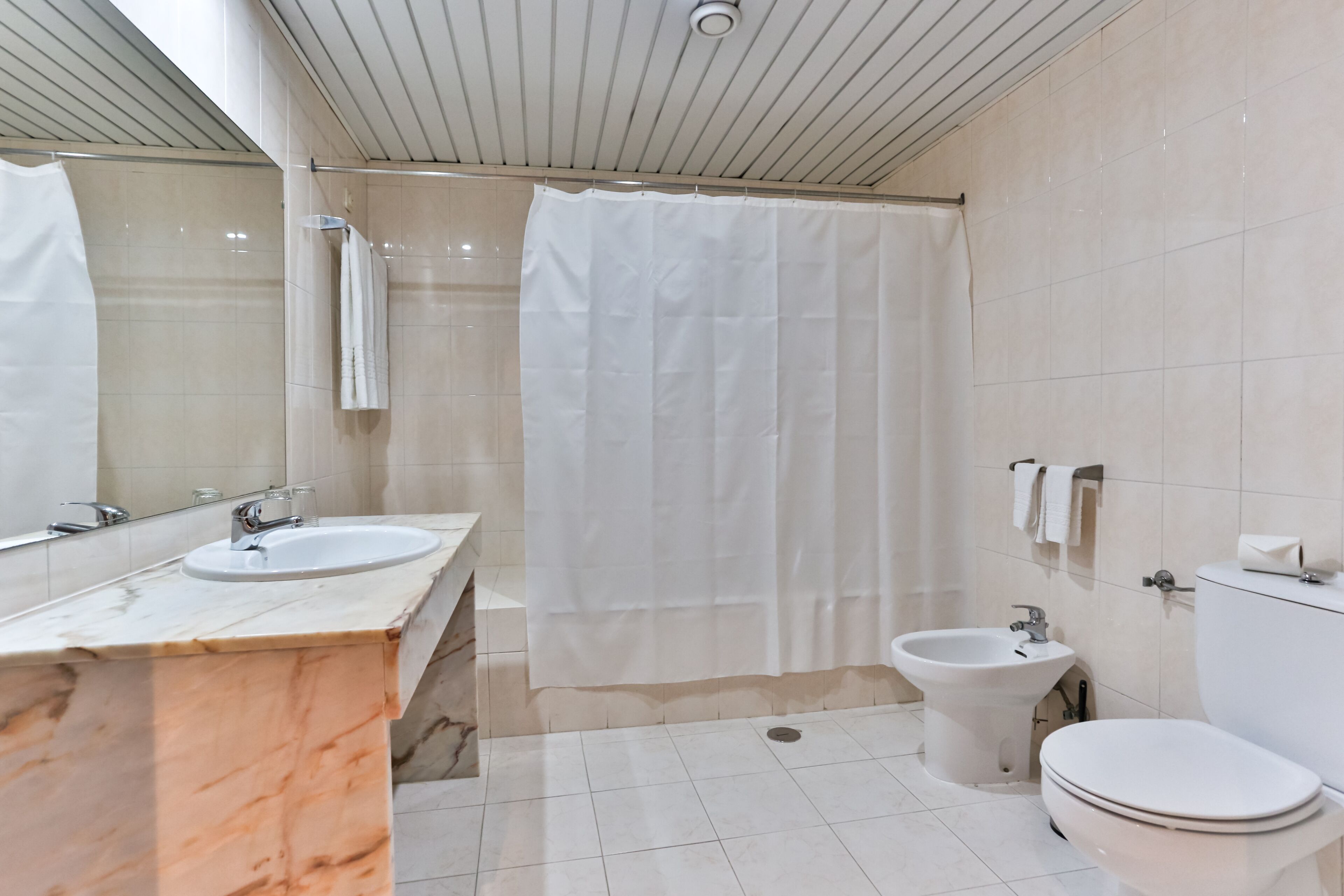 Um banheiro moderno com pia de mármore, bidê, vaso sanitário e cortina de chuveiro.