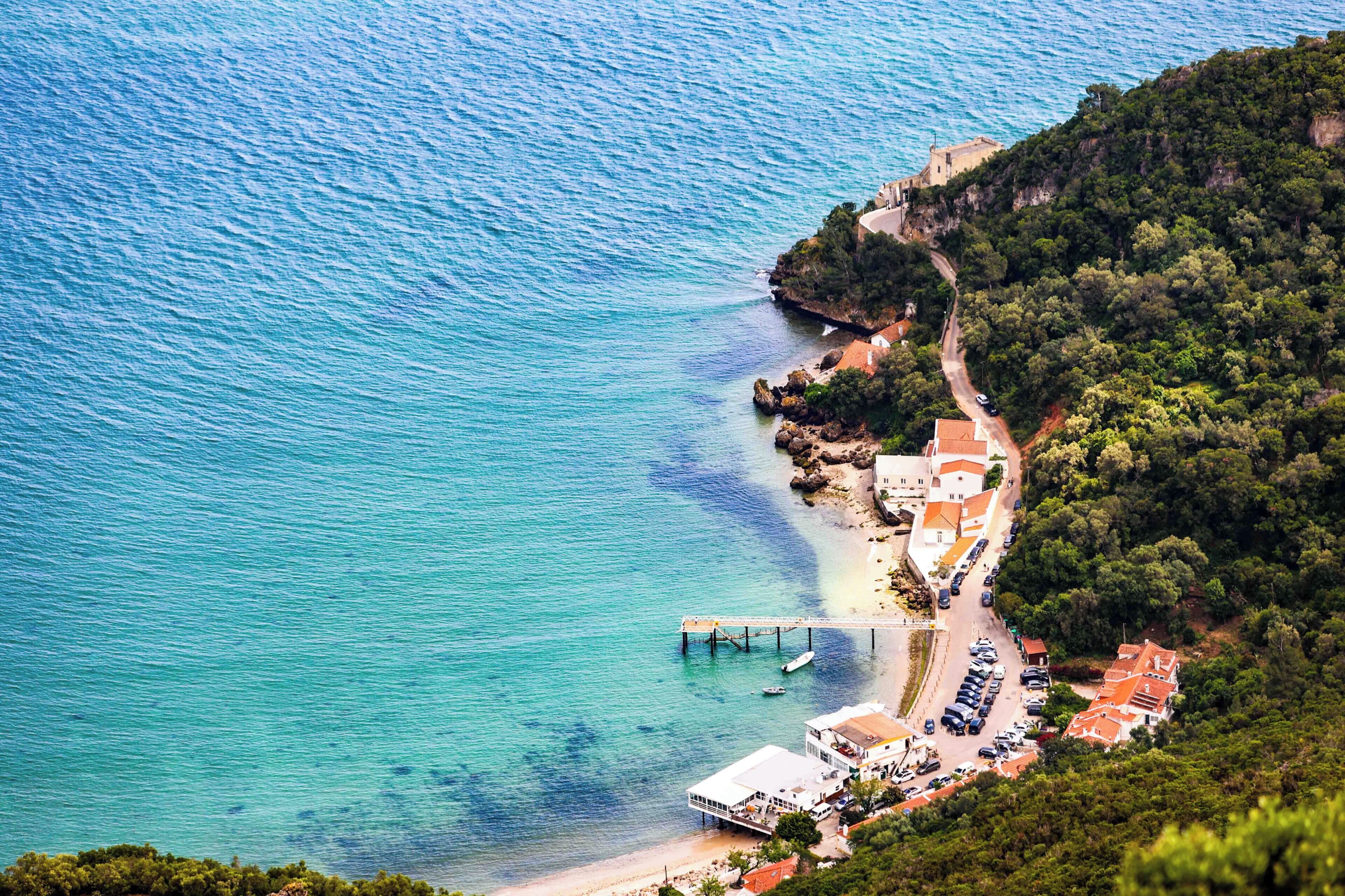 A coastal area with a beach, a pier, and buildings with red roofs.