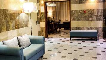 A hotel room with a sofa, a bench, a dining area with chairs and a table, and a patterned floor.