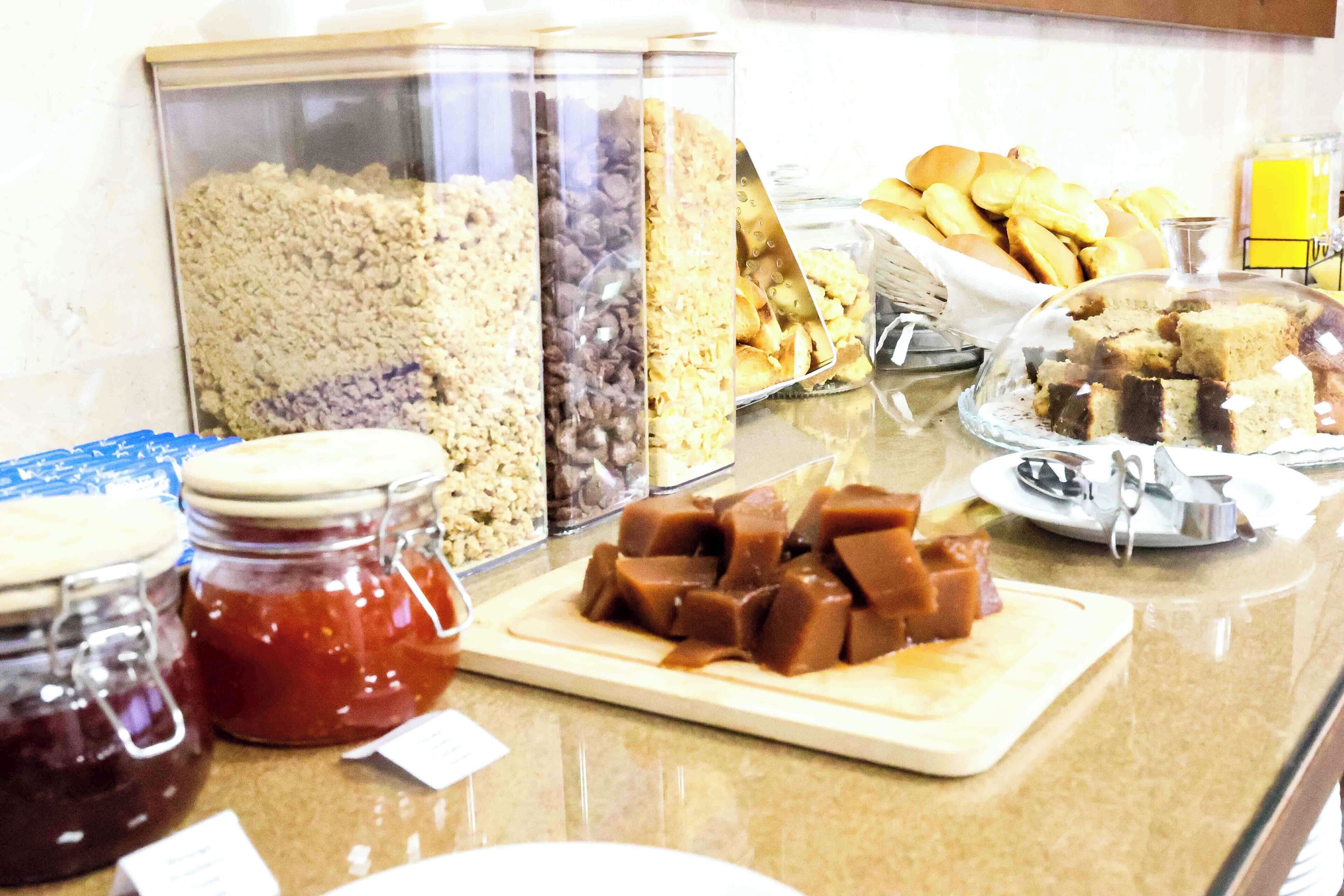 En buffet med et udvalg af mad, herunder syltetøj i glas, en tallerken med brownies og en beholder med småkager.