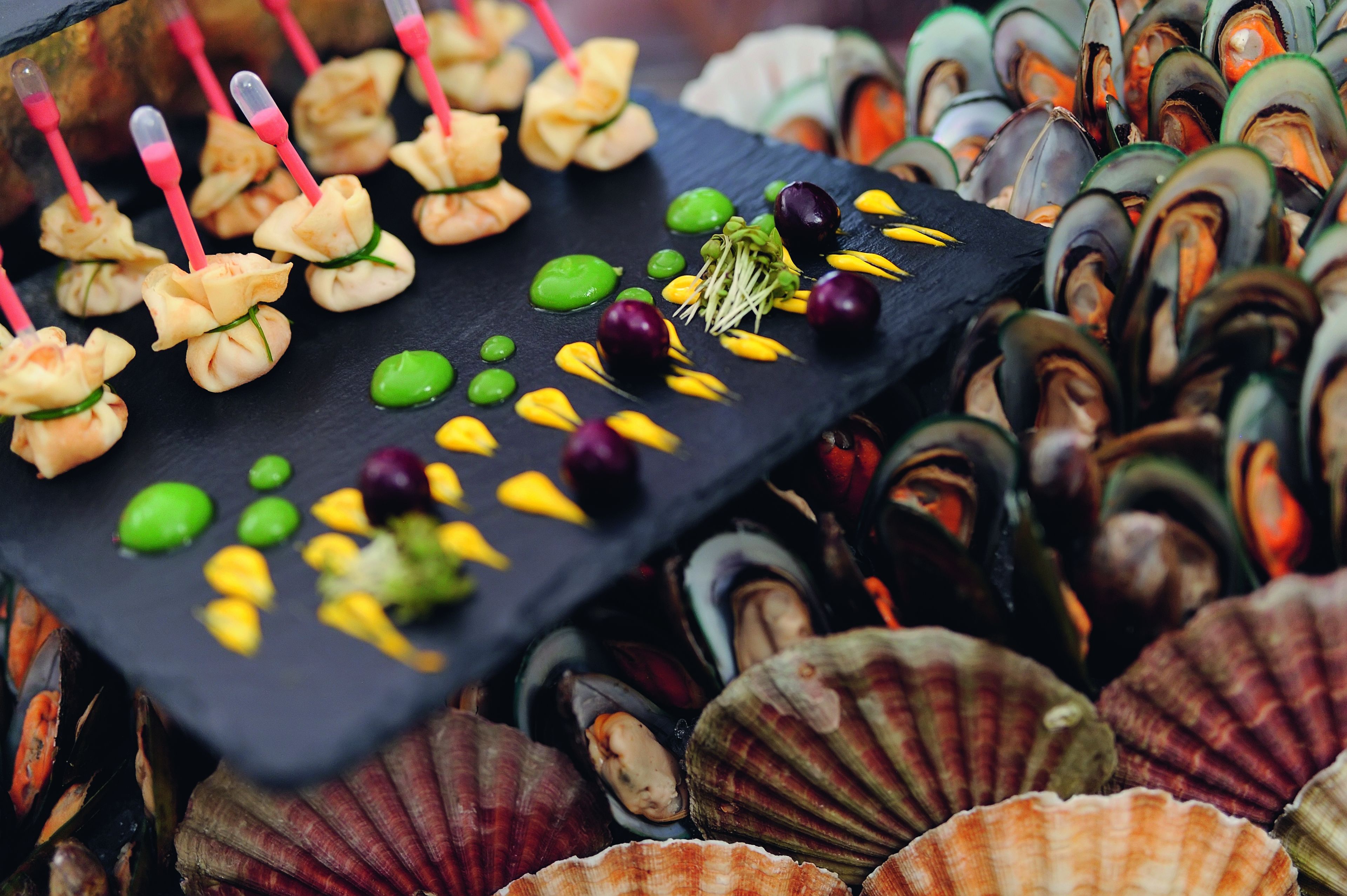 A variety of seafood, including mussels and scallops, arranged on a black slate board.