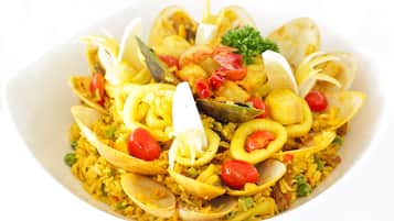 A bowl of seafood paella with clams, shrimp, and vegetables.