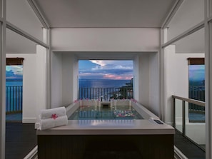 Un espace spa offrant une vue sur la mer et le paysage urbain, avec une baignoire et une serviette posée sur le comptoir.