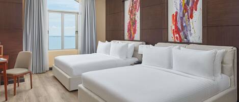 Habitación de hotel con dos camas, un escritorio y una silla. Cuenta con un ventanal con cortinas y cuadros en las paredes.