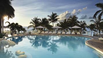 A pool with lounge chairs and umbrellas, surrounded by palm trees.