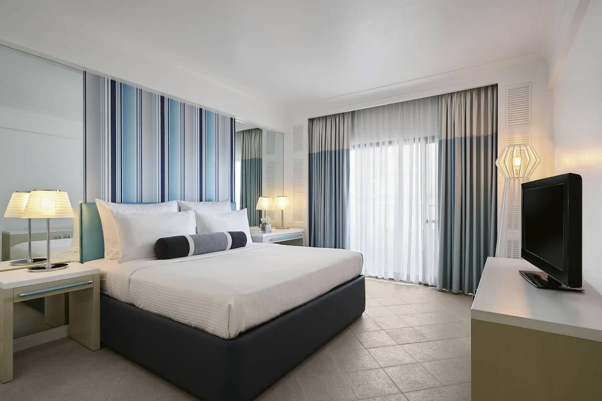 A modern hotel room with a large bed, bedside tables, a flat-screen TV, and a view of the outdoors.