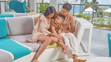 Family relaxes on a wicker sofa with a view of palm trees and water.