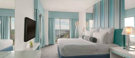 Habitación de hotel con cama, escritorio, televisión y balcón con vistas.