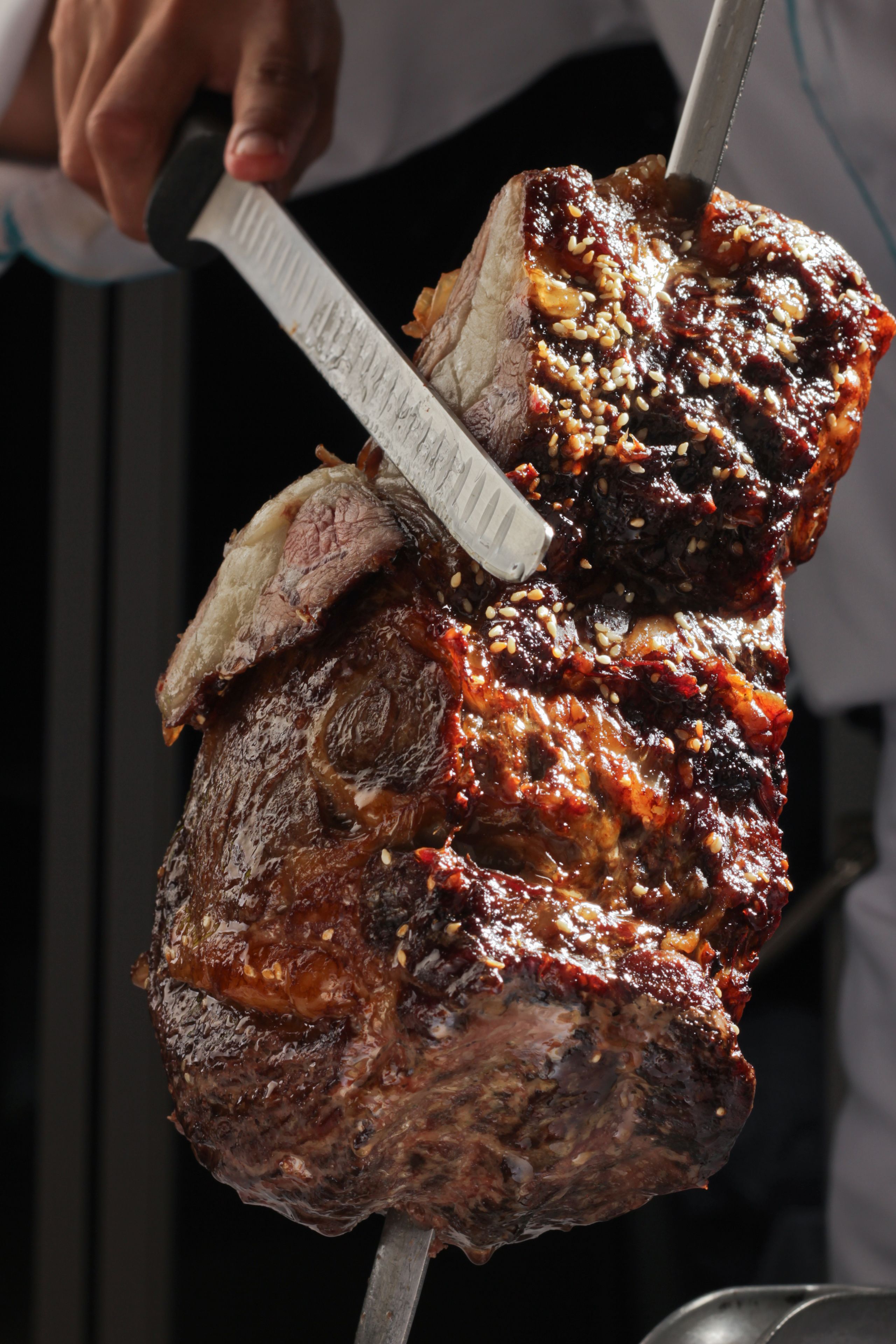 A large, roasted meat on a skewer being cut by a person.