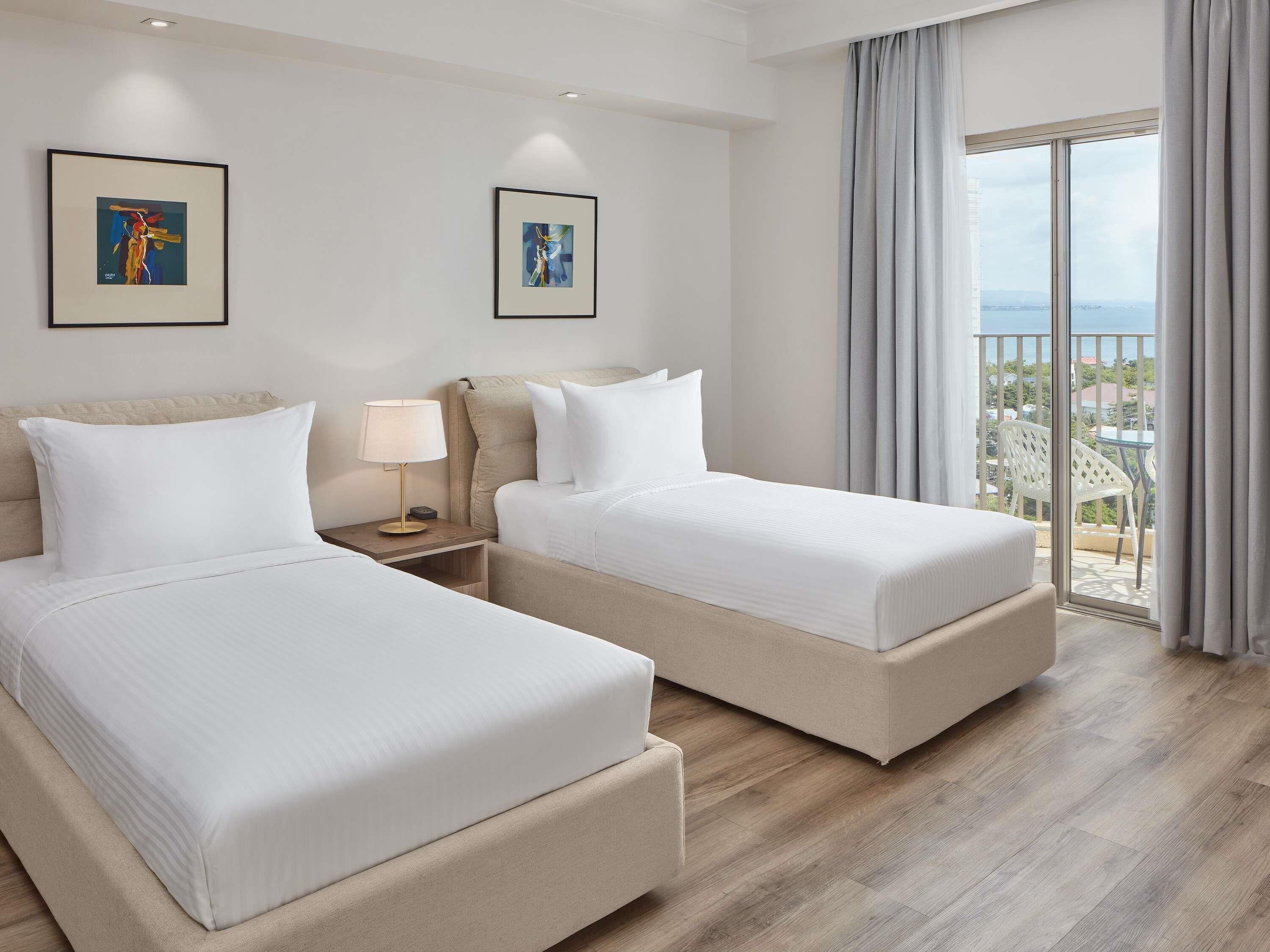 Habitación de hotel con dos camas, una mesita de noche, una lámpara y dos obras de arte enmarcadas en la pared.