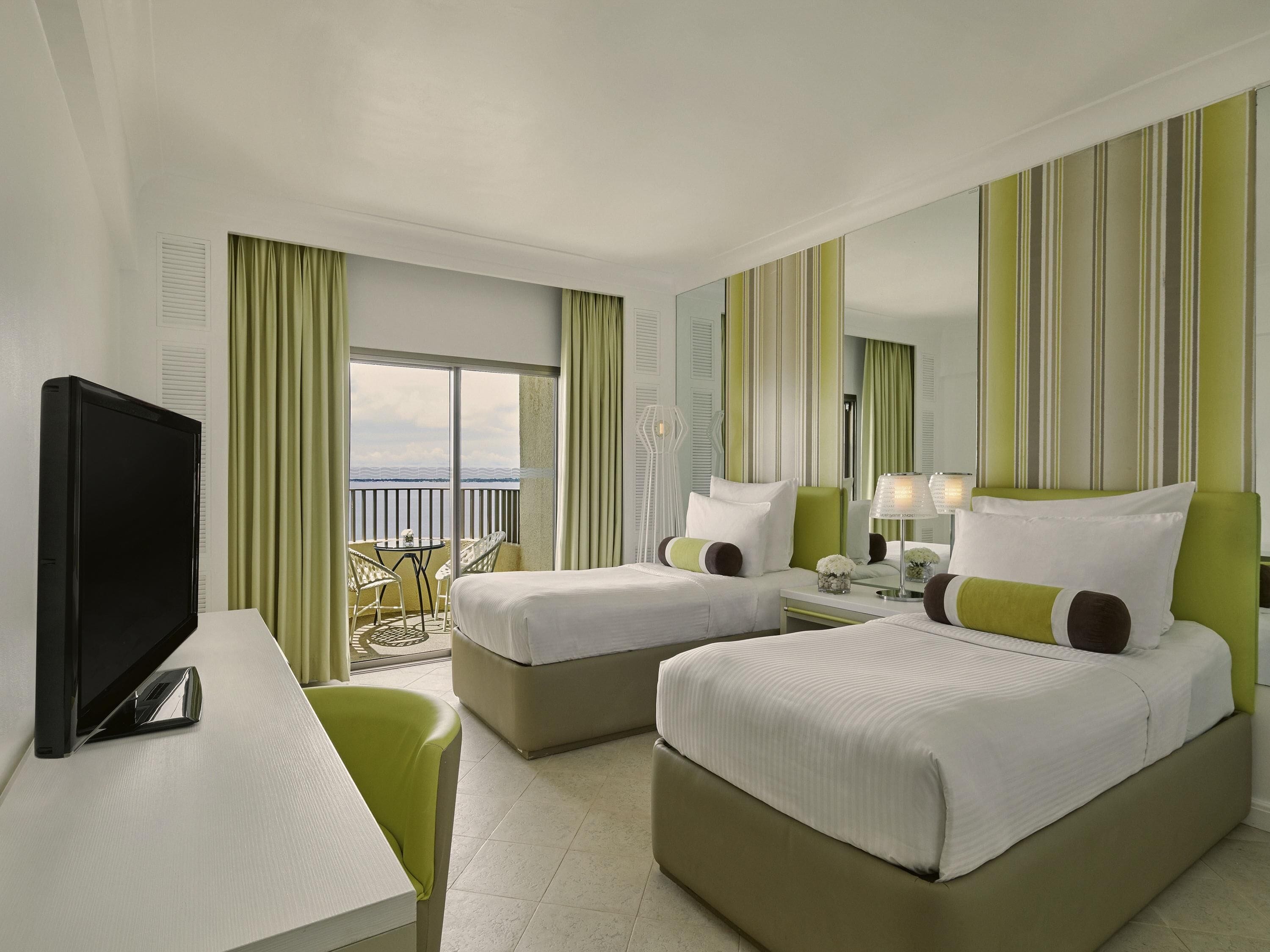 Habitación de hotel con dos camas, televisión, escritorio y balcón con vistas.