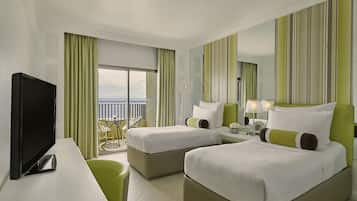 Habitación de hotel con dos camas, televisión, escritorio y balcón con vistas.