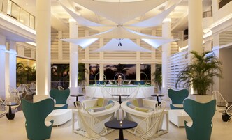 A spacious lobby with high ceilings, white columns, and a central fountain. There are several seating areas with white and green chairs.