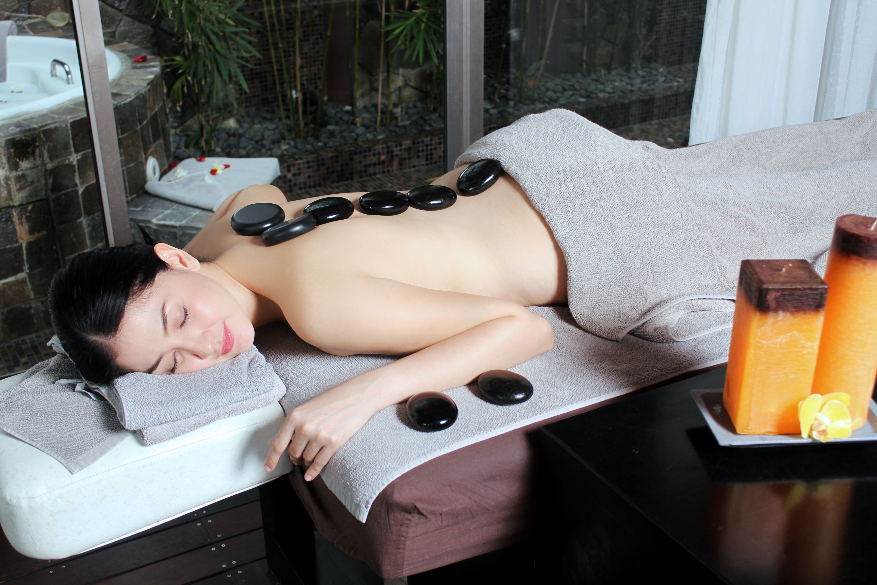 A massage therapy session with a stone massage table, a towel, and a tray with candles and a fruit slice.
