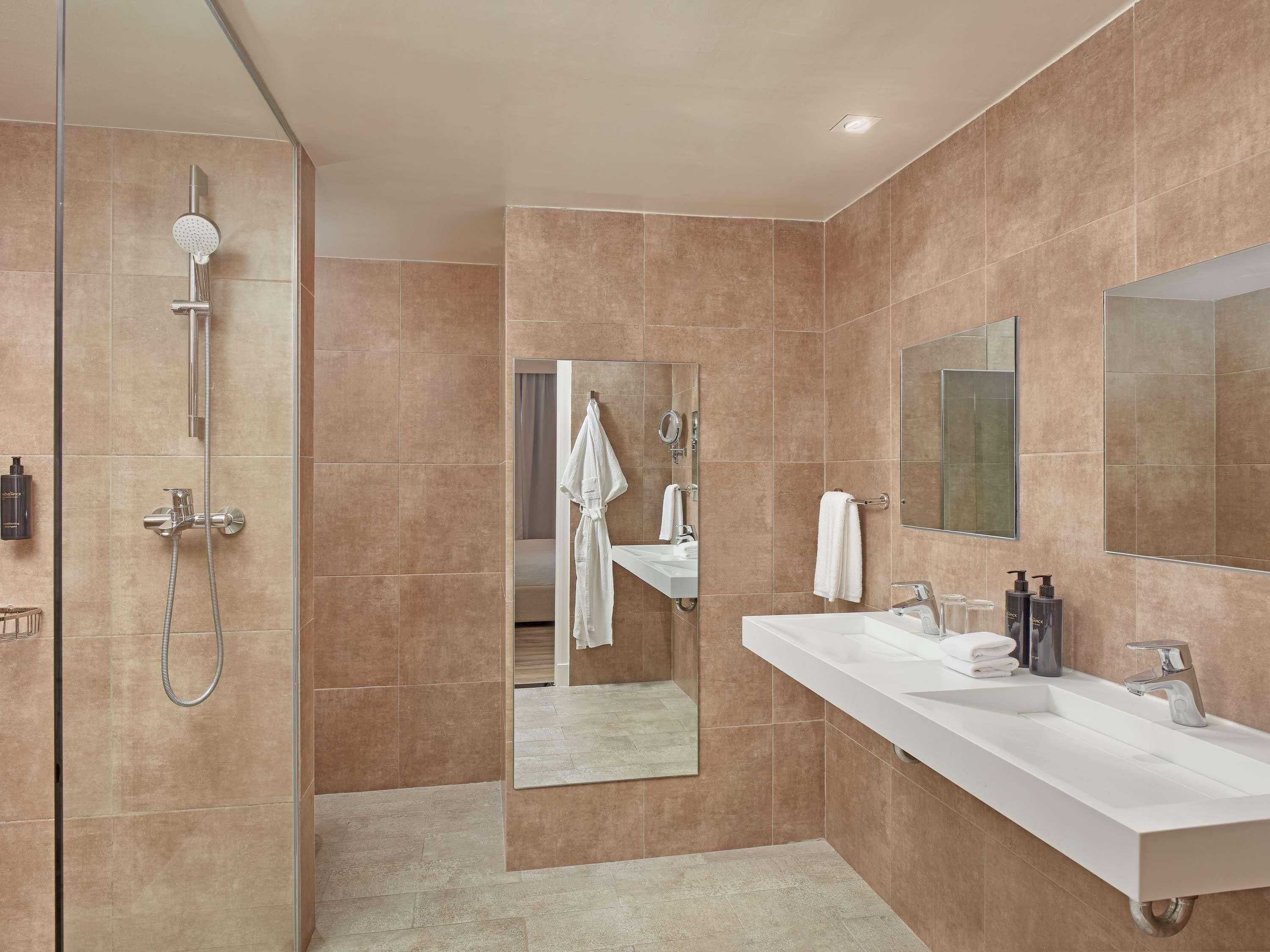 Un baño moderno con ducha envuelta en vidrio, un espejo grande y un tocador blanco con lavamanos.
