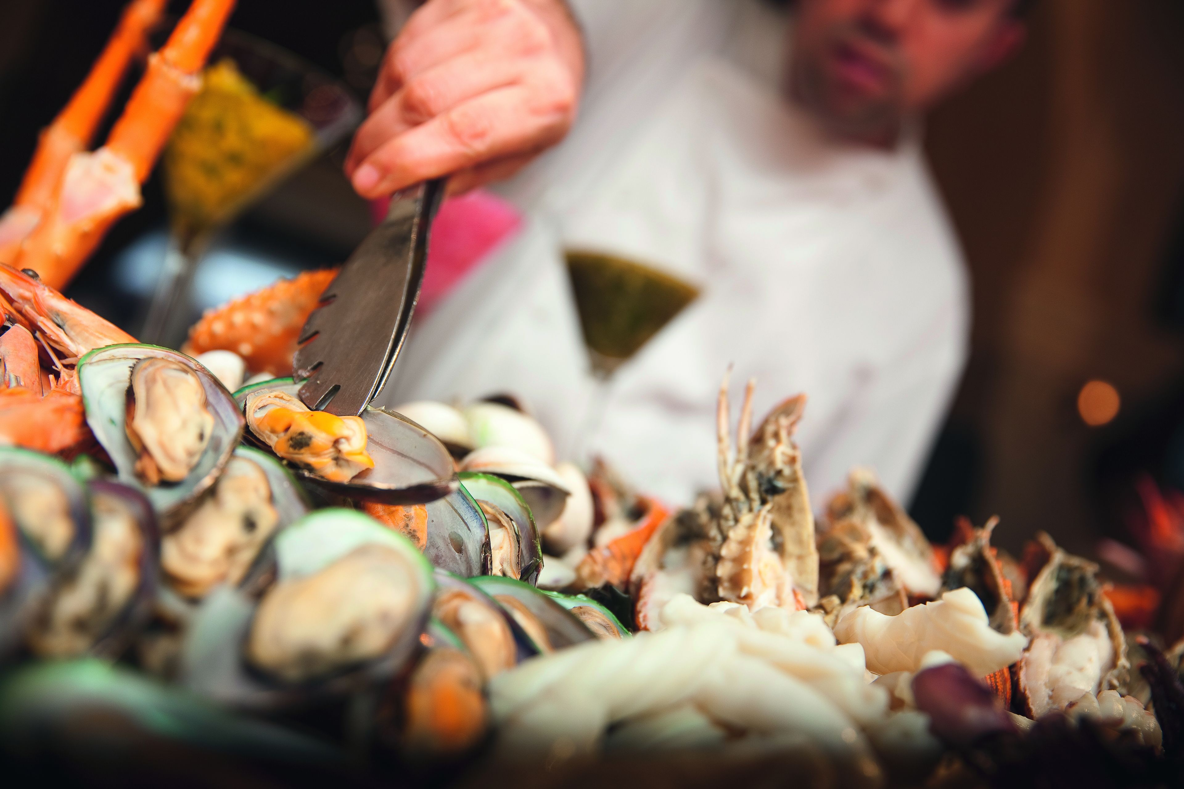 A variety of seafood including clams and shrimp, with a person using tongs to handle the food.