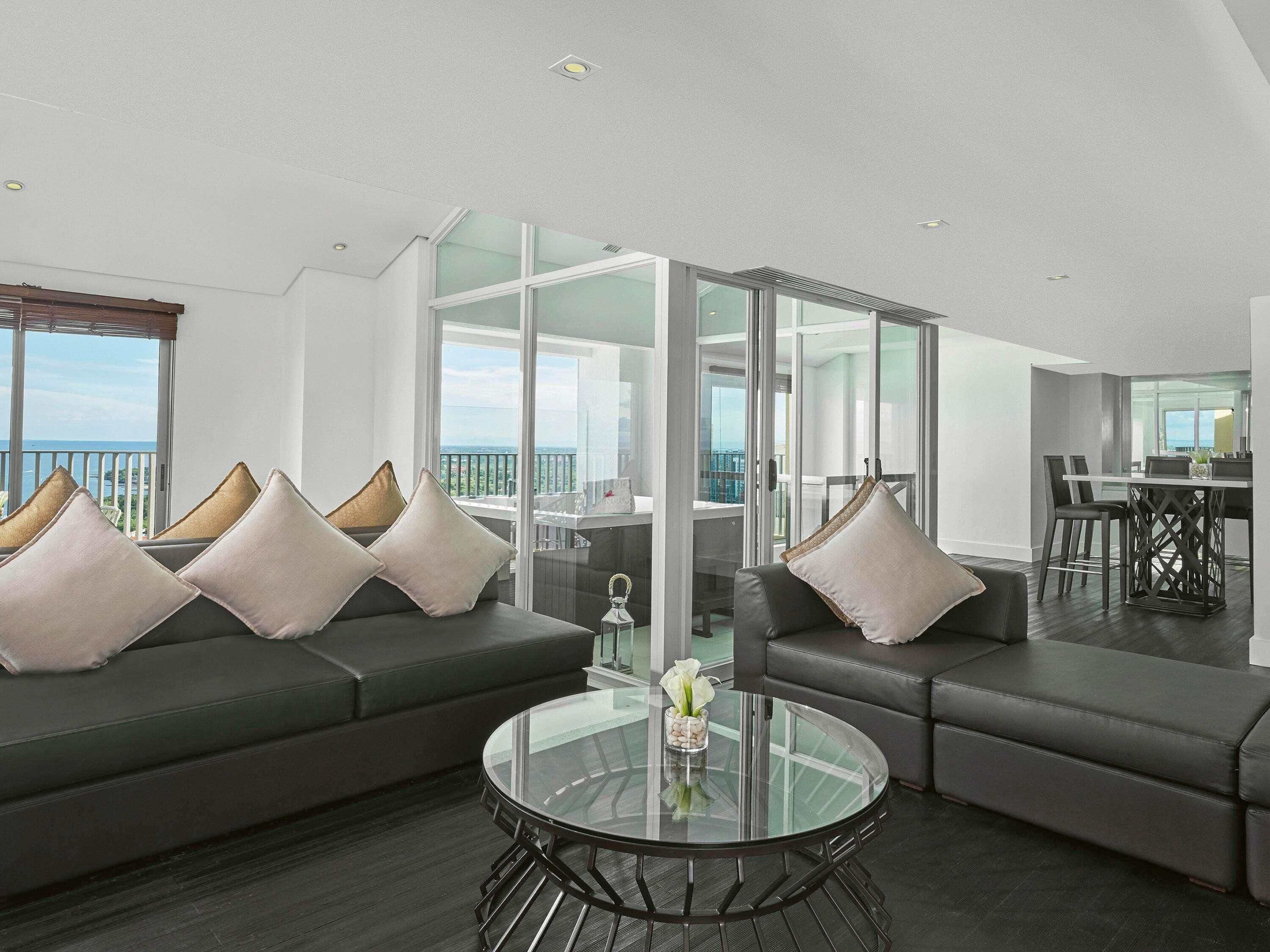 Una sala de estar moderna con una mesa de centro de vidrio, sofás de cuero oscuro y vistas al mar a través de amplios ventanales.