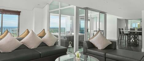 Una sala de estar moderna con una mesa de centro de vidrio, sofás de cuero oscuro y vistas al mar a través de amplios ventanales.